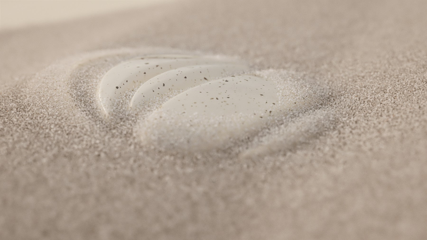 A close-up view of sand with visible texture and grains, featuring a footprint imprinted in the surface